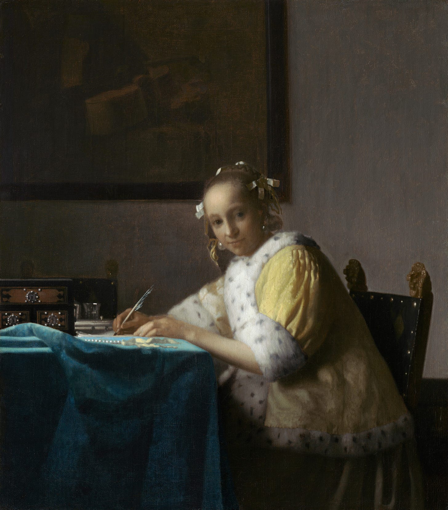 a woman with white ties in her hair wears a white and yellow frock and sits with a pen in her hand while she writes a letter at a table covered in a blue cloth