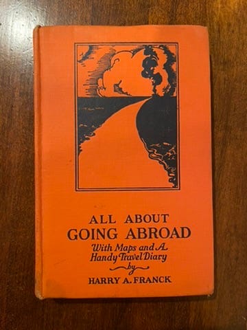 A small orange-covered book. There's a black print of a road arcing towards a cloudy horizon. Title: All About Going Abroad With Maps and a Handy Travel Diary by Harry A. Franck.