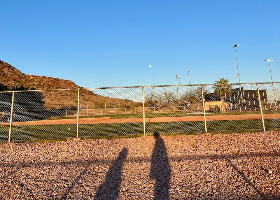 A view of the moon over a baseball field, with the shadows of myself and my daughter