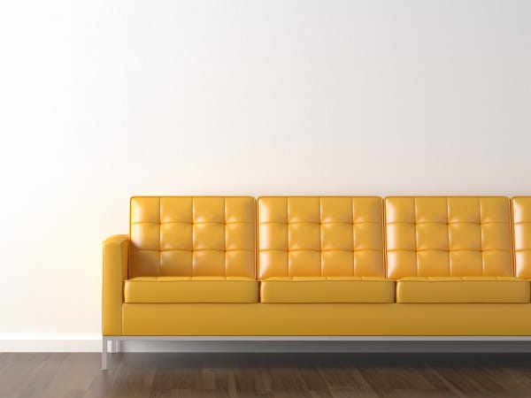 Tufted yellow leather couch against a blank white wall