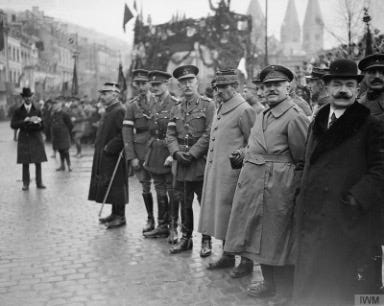 Black and white photo of the World War I Allied Armistice Commissioners in November, 1918. They are standing on a street in uniforms with other people standing in the background. The Commissioners are Lieutenant General Richard Haking (British), General Alphonse Nudant (President and French representative), and General Hector Delobbe.