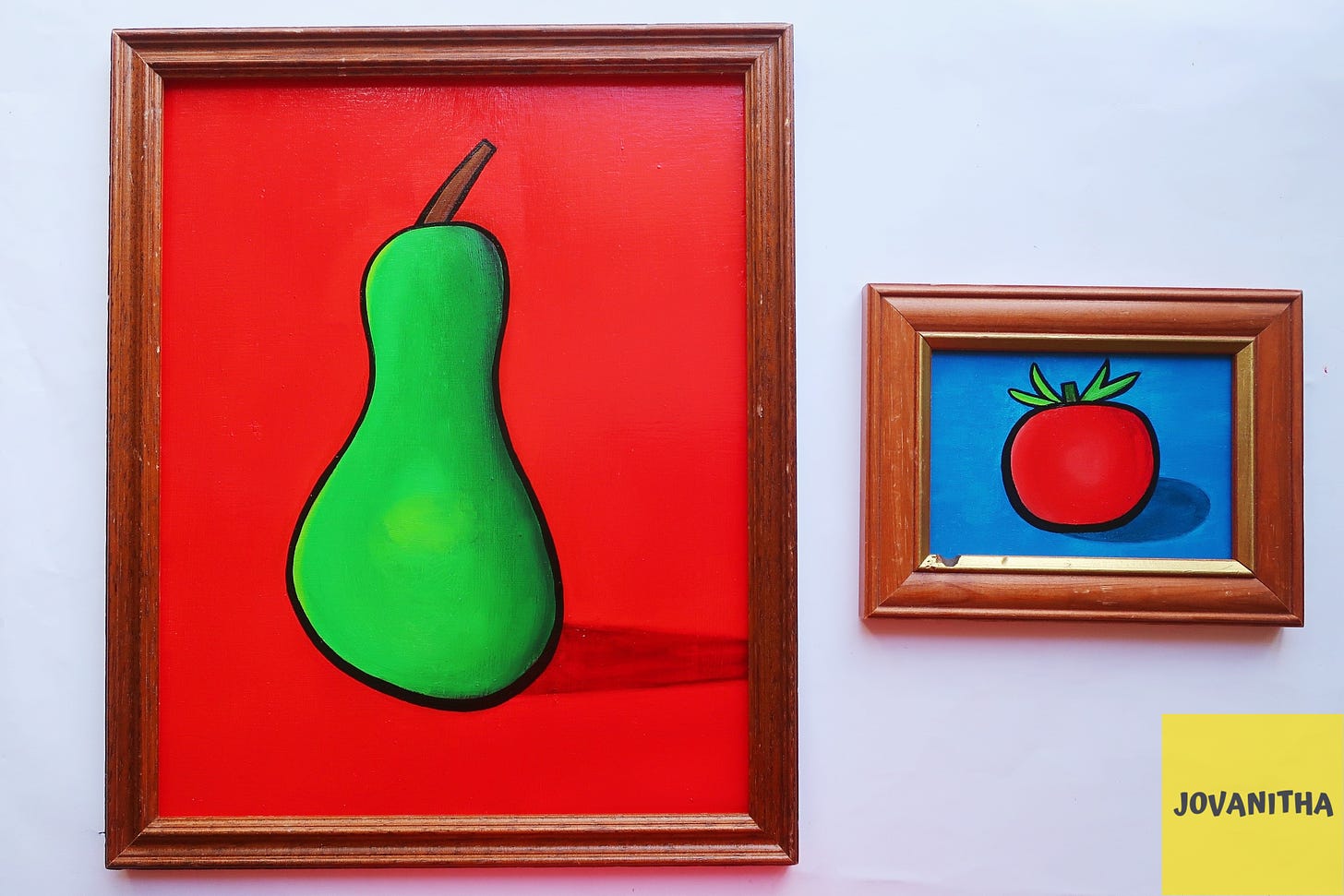 An oil painting of a green pear on a red background in a thrifted frame and a red tomato on a blue background in a thrifted frame