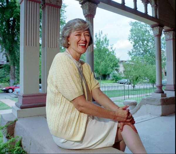 Patricia Schroeder sitting outdoors, smiling for a portrait. A suburban street scene is in the background.