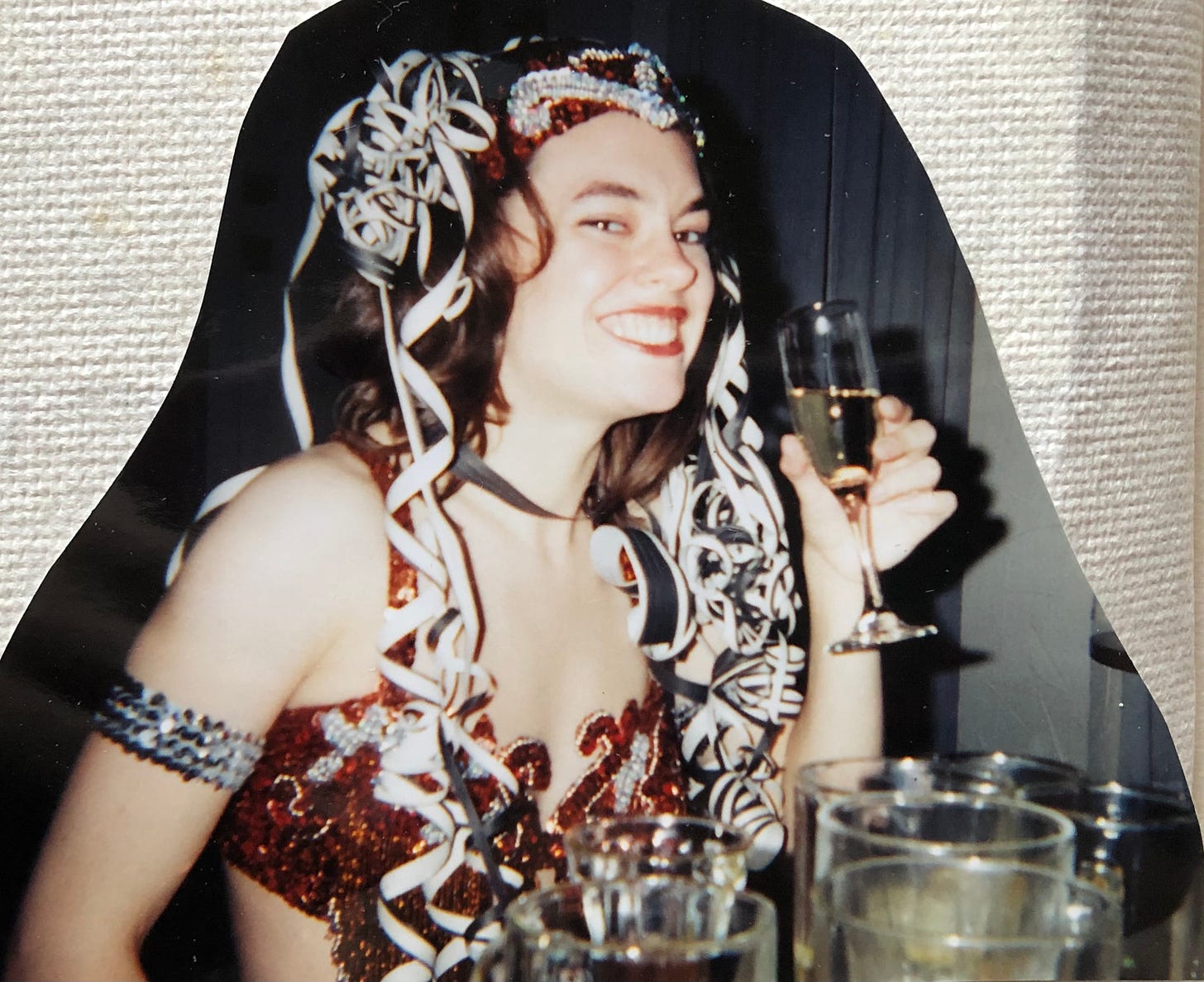 The author in a copper and silver belly dance costume, complete with a champagne flute, a fountain of curly silver streamers in her hair, and a huge grin.
