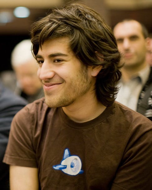 A young man with a few days' beard growth, in a brown shirt, smiling, facing slightly to the left of the camera.