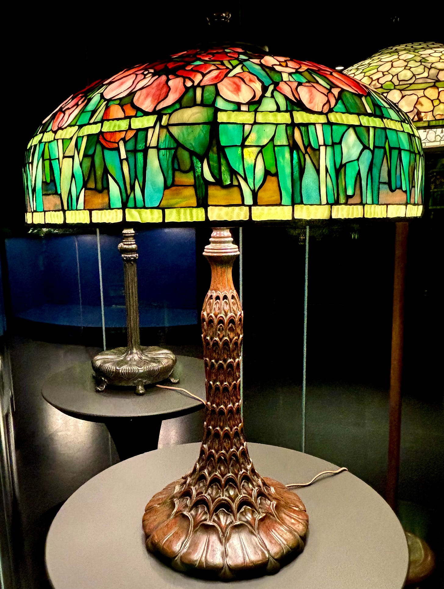 A glass lampshade that is a mosaic of red tulips atop an ornate base.