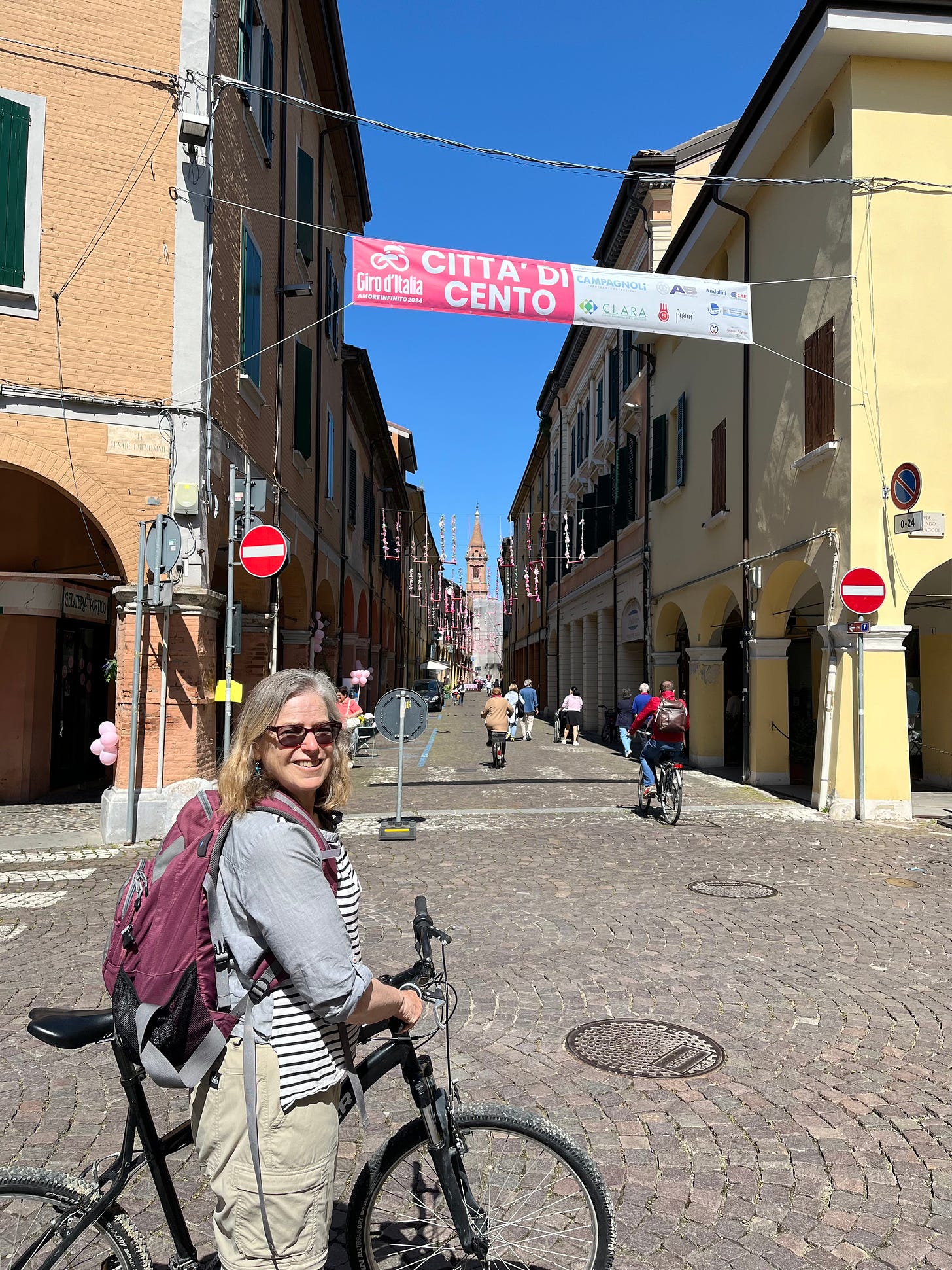 Woman holding bike in front of a narrow street in a small Italian town.