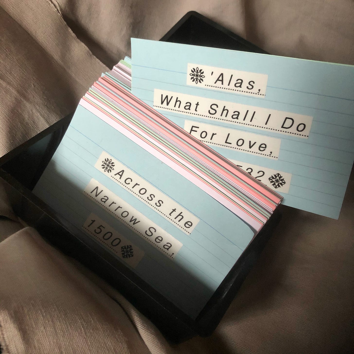 A black box of index cards, two are visible and read “Across the Narrow Sea, 1500” and “Alas, What Shall I Do For Love”