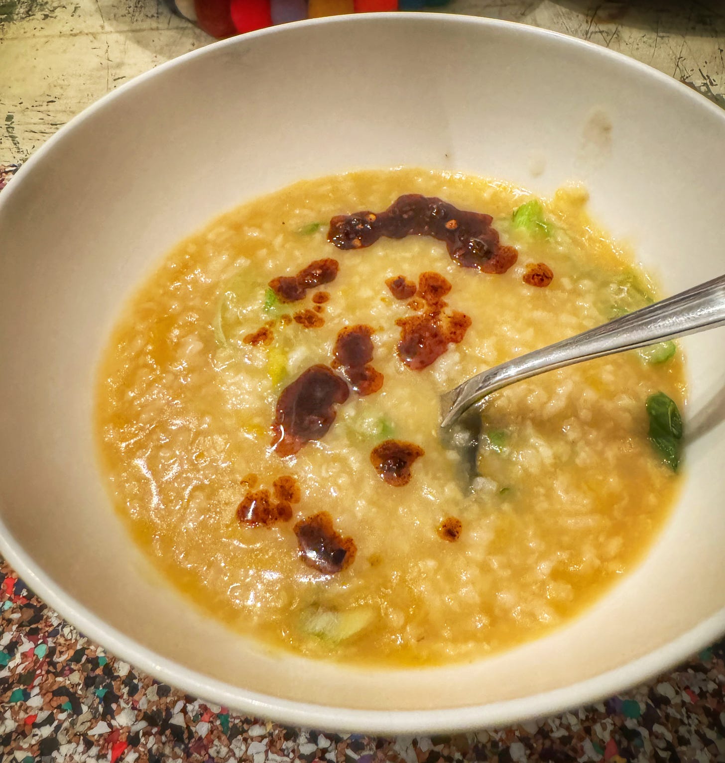 A bowl of butternut squash congee, topped with sliced green onion and a splash of chili crisp