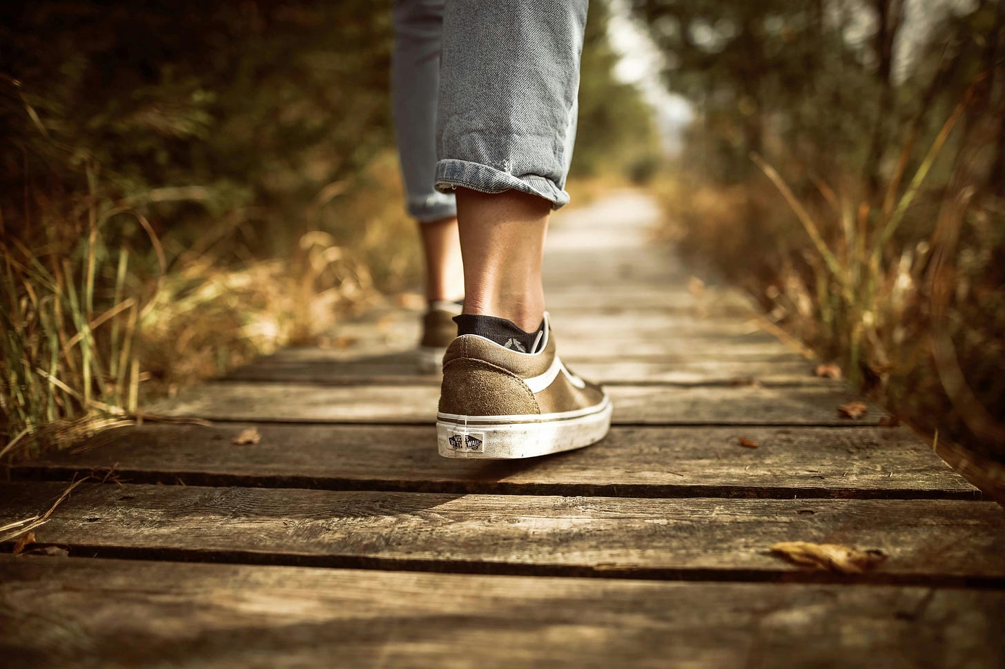 person in vans tennis shoes walking a wooden boardwalk path in the nature