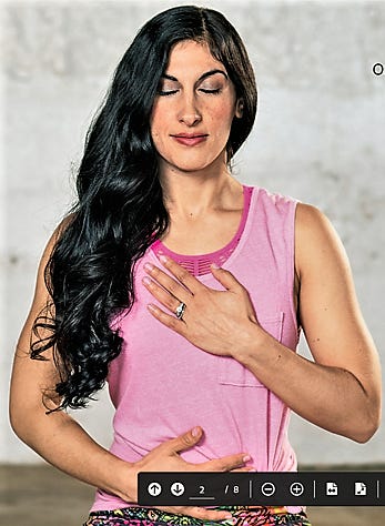 Picture of a woman in a pink shirt, with long dark hair; her left hand rests on her chest, and her right hand on her abdomen. She's checking in with her body.
