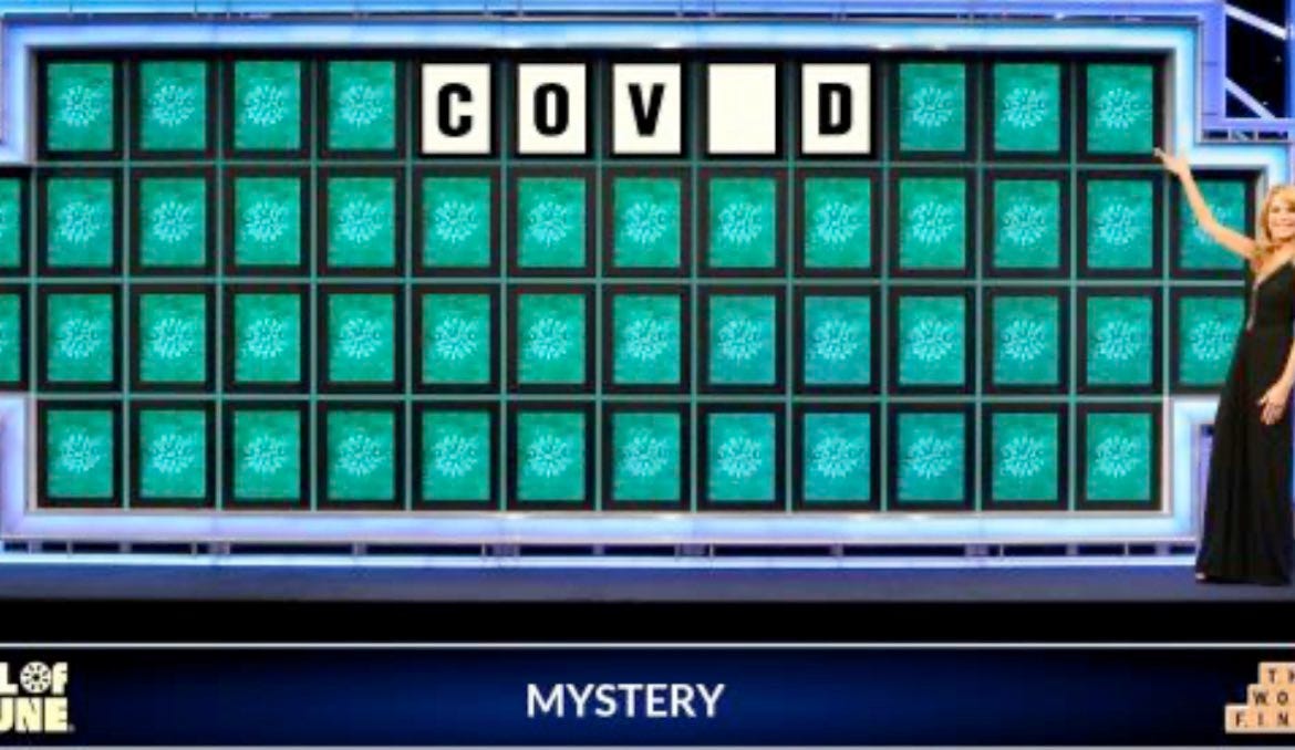 The image is from Wheel of Fortune the word puzzle tv game show with a formally dressed blonde pointing at the mystery word that is on the big board spelled C, O, V, missing letter, D. And the caption underneath says MYSTERY. 