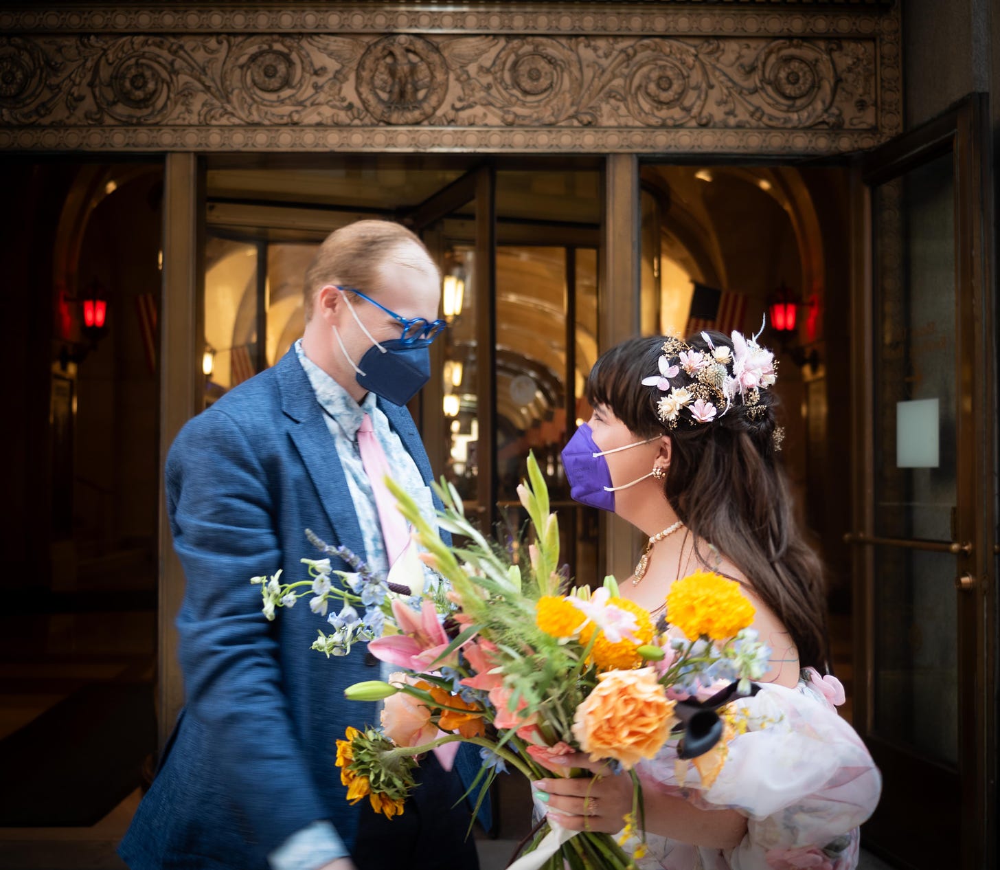 Daniella and her partner Joe stand smiling at each other behind face masks outside of Chicago's city hall, wearing their wedding garb.