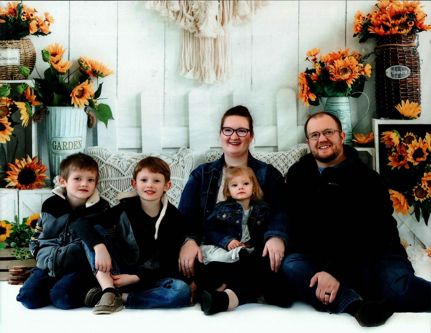 smiling man and woman with glasses and three small children in posed photo with potted sunflowers