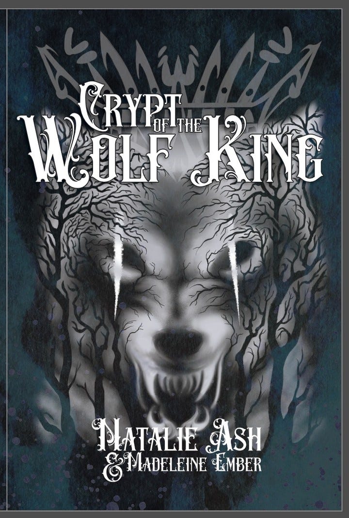 Image of the front cover of a book. The title reads "Crypt of the Wolf King" and credits "Natalie Ash & Madeleine Ember". There is an image of a ghostly wolf face and silhouettes of trees.