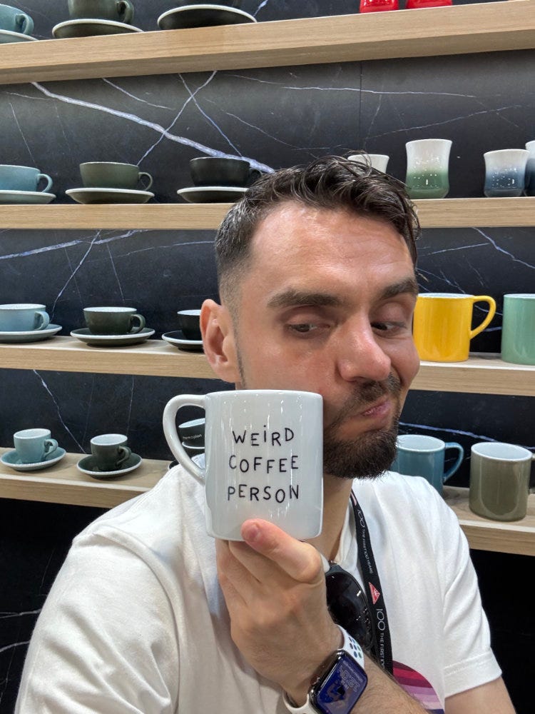 Na zdjęciu ja, trzymający kubek z targów World of Coffee 2024, z napisem: „Weird Coffee Person”.