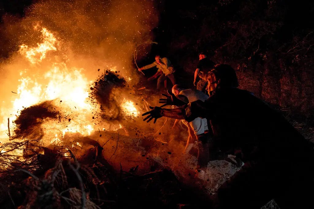 Residents of Canakkale in Turkey throw dirt onto flames in the dark of night, during a wildfire in August 2023.