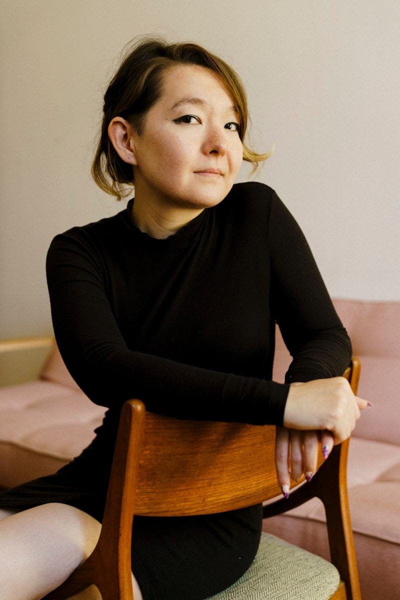 Artist photo of Patty Kim Hamilton, seated backwards on a wooden chair