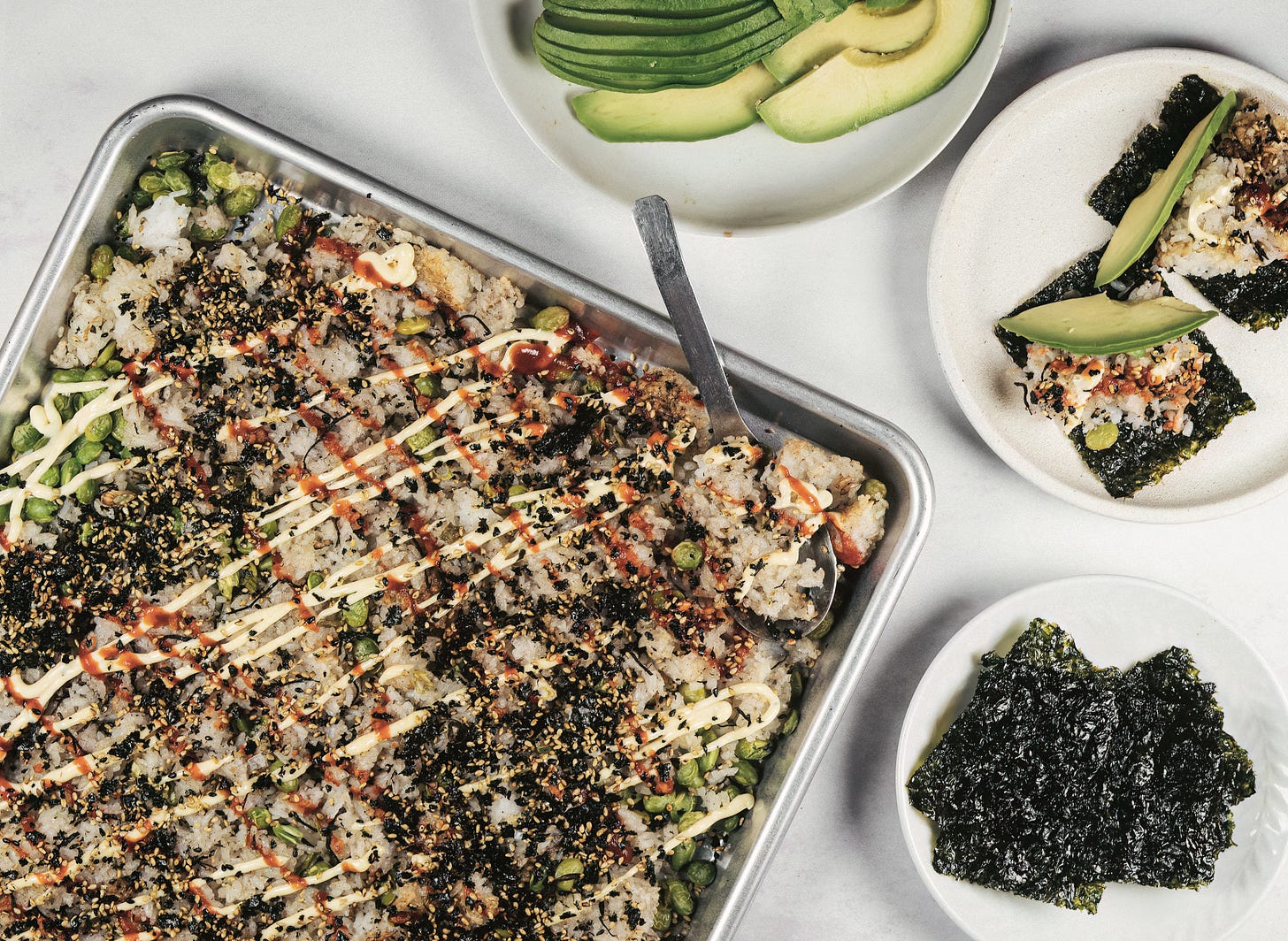 baked rice on a sheet pan with plates of avocado and nori