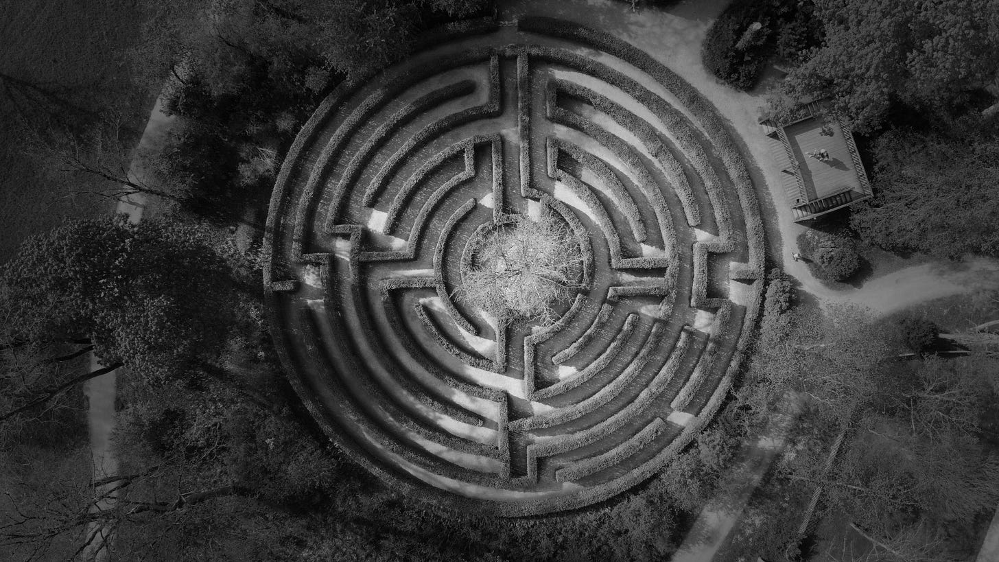 A black-and-white aerial photograph of a labyrinth formed by hedges.