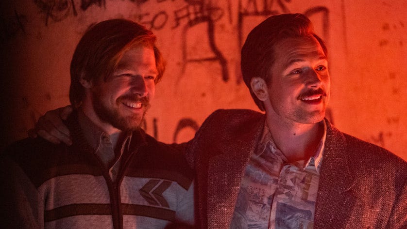 Nikita Efremov and Taron Egerton smiling next to each other in a scene from the film Tetris.
