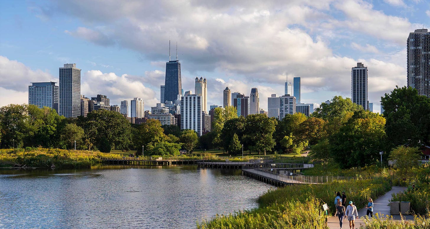 Chicago skyline pictured from a nearby public park with a lake, greenery and trails.