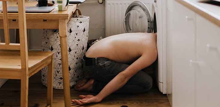 Photo of man who has fallen asleep while his head is in an open washing machine.