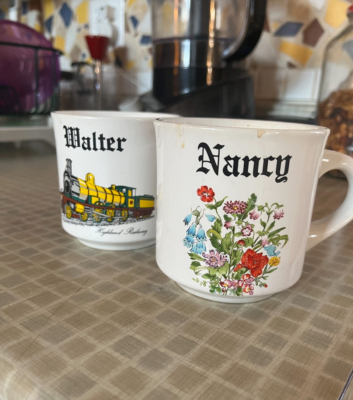 A pair of mugs. One has the name "Nancy" and has flowers on it. The other says "Walter" and has a train.