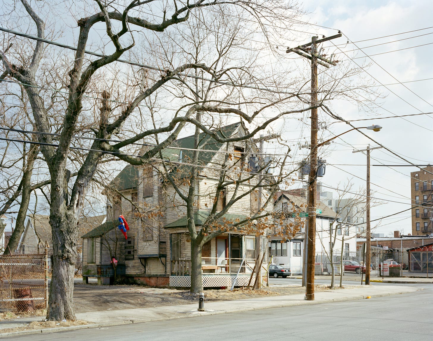 House in Far Rockaway with leafless trees and telephone poles in front. A decapitated superman doll hangs from a tree.