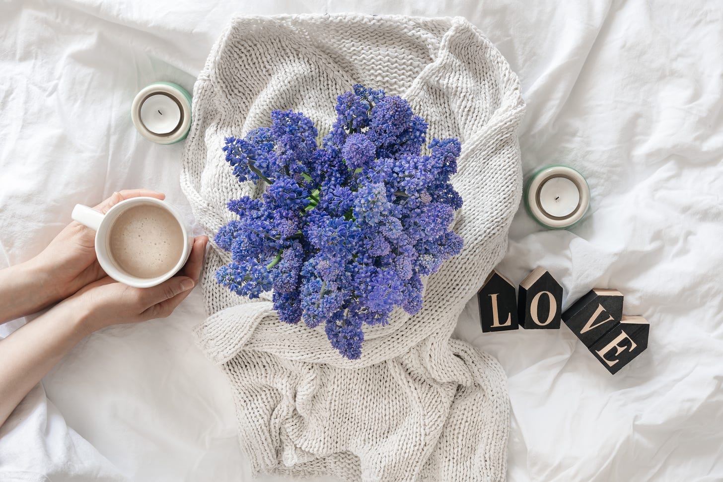 A bouquet of flowers a cup of coffee and a decorative word love in a white bed