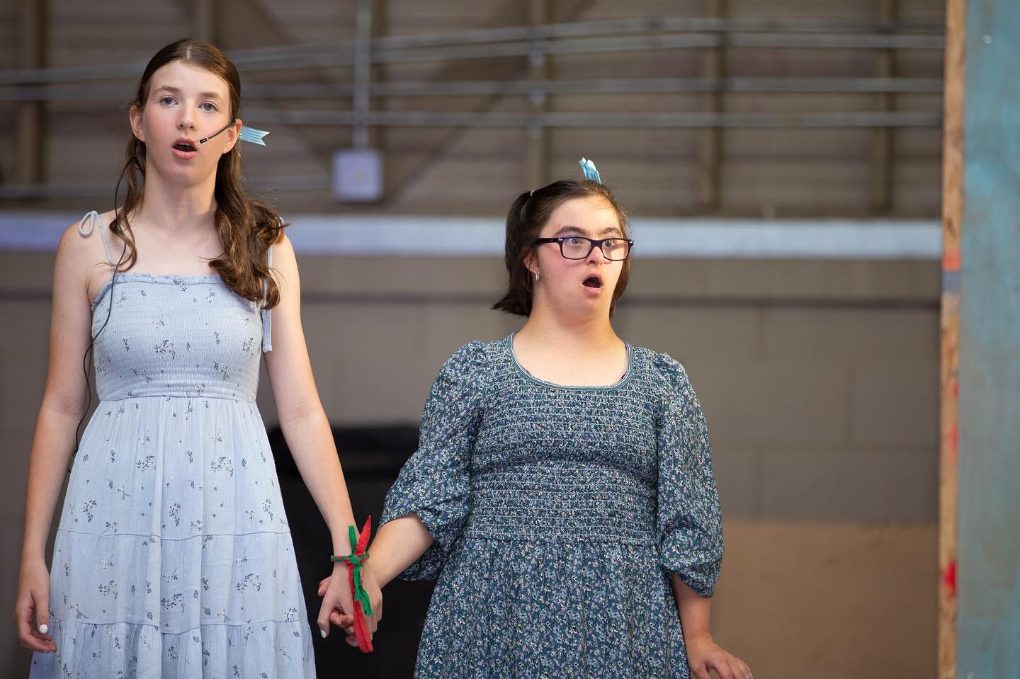 Two female teenage campers hold hands and sing onstage