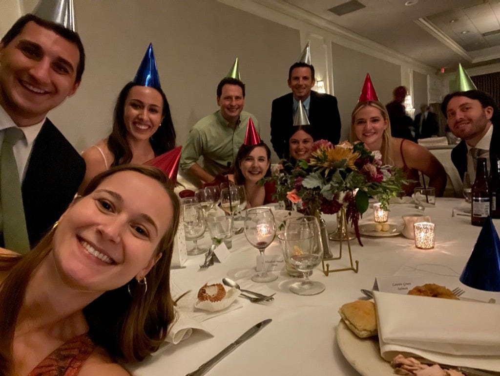 Photo of myself and 8 friends in party hats at a wedding.