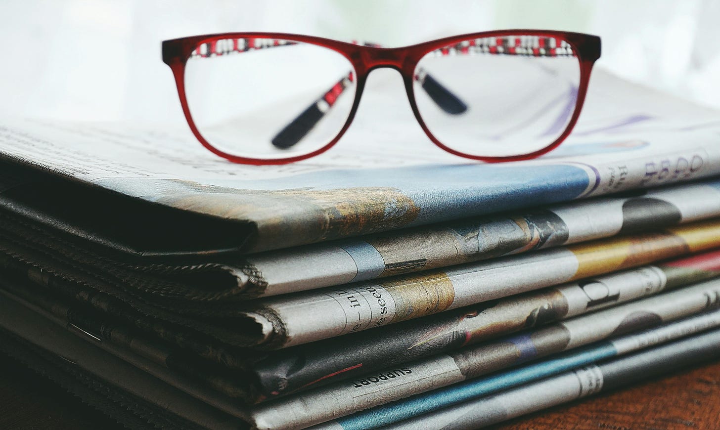 A pair of red-framed eyeglasses on a stack of newspapers.