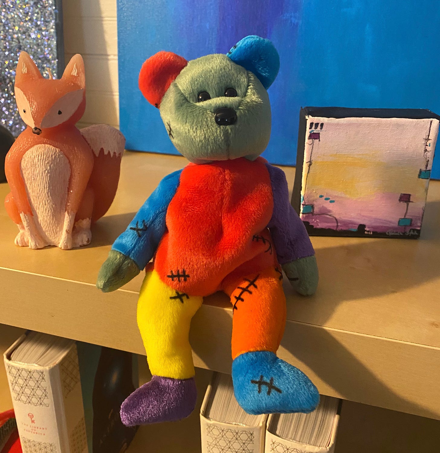Frankenstein-themed Beanie Babie sitting on a shelf with a wax fox and small purple painting behind it.