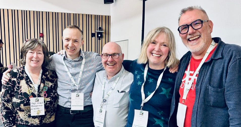Five grinning people on an adrenaline comedown after a fast and furious Gasta (see article). All wearing conference lanyards and clearly in some sort of lecture theatre.