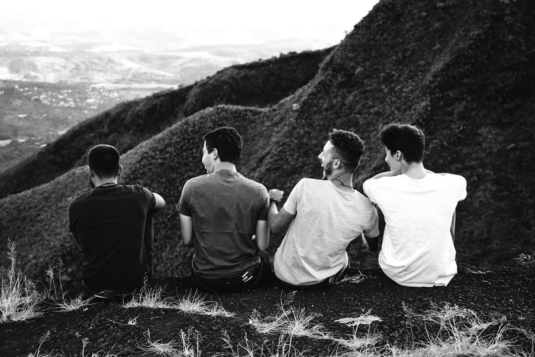 row of four men sitting on mountain trail row of four men sitting on mountain trail
