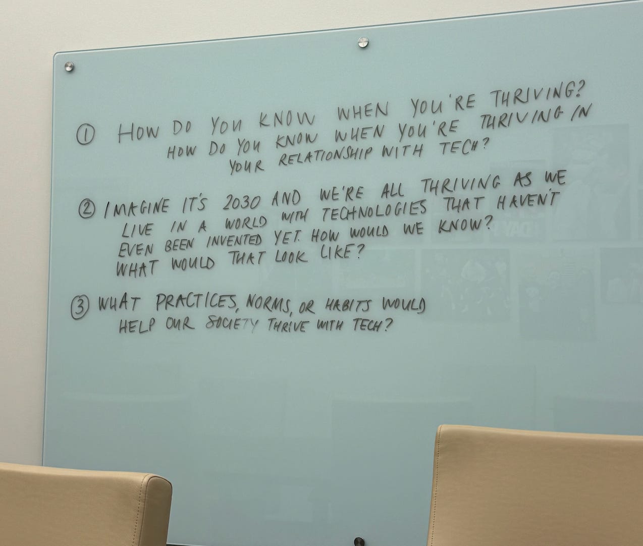 A glass board with written questions about thriving with technology.