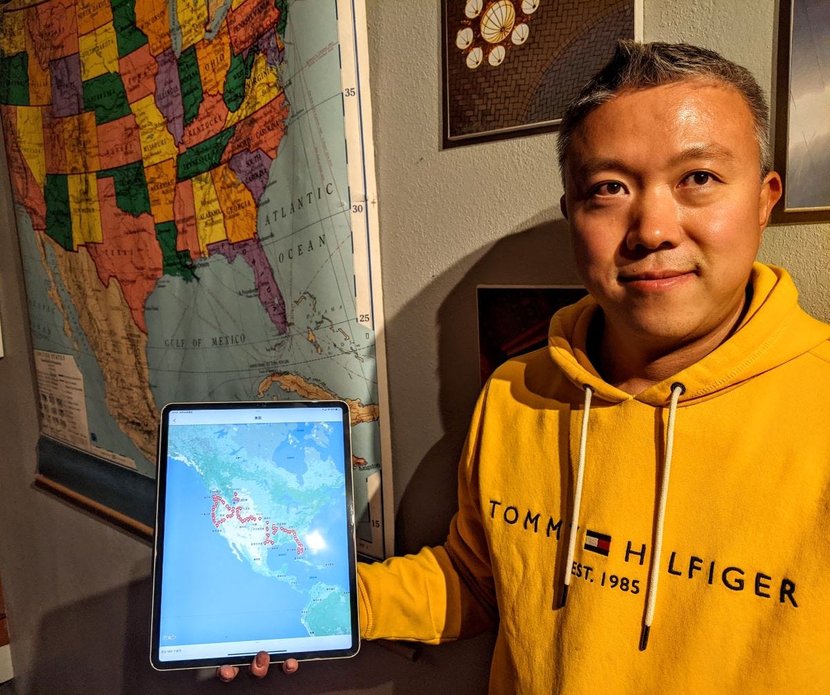 a man holding an iPad showing a map of the USA with red dots in front of a large hanging USA map on the wall