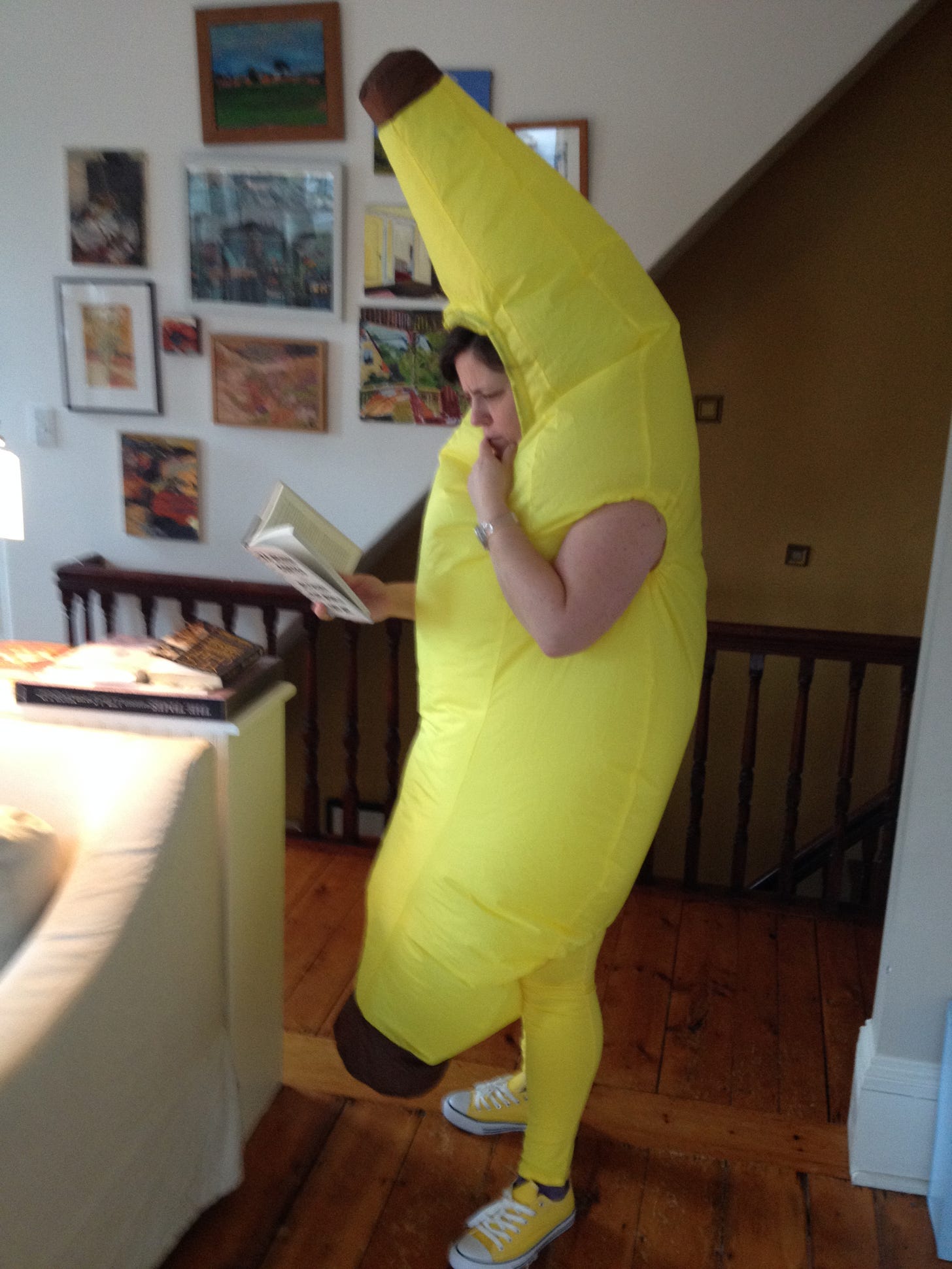 Phoebe Potts reading a book with a puzzled expression, wearing a giant banana costume.