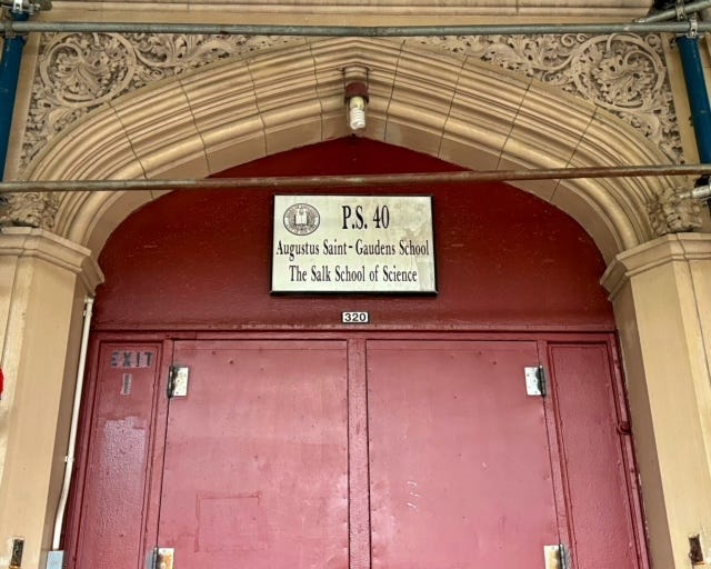 A red door under an engraved archway (which is under construction scaffolding). A sign over the entrance reads P.S. 40 Augustus Saint-Gaudens School The Salk School of Science.