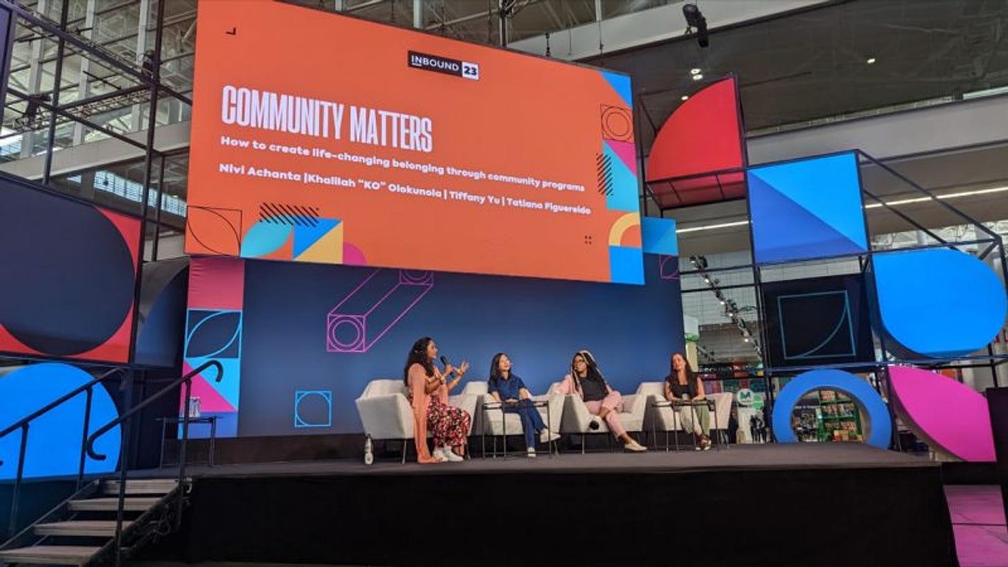 Nivi, Tiffany, KO, and Tatiana seated on stage with an orange slide on the screen behind them that reads: “Community Matters: How to create life-changing belonging through community programs”