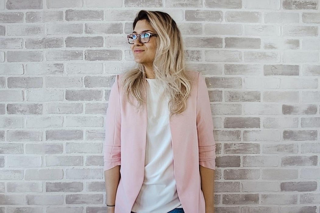 Woman standing in front of a brick wall wearing a pink cardigan