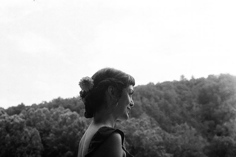 a black and white photo of me looking to the side, with the mountains behind me. I am smiling. 