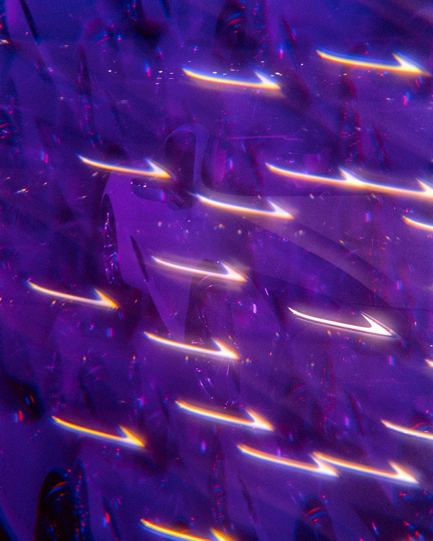 A kalideoscopic style image flooded with purple, little rainbow reflections, and a repeat image of the headlight of the car