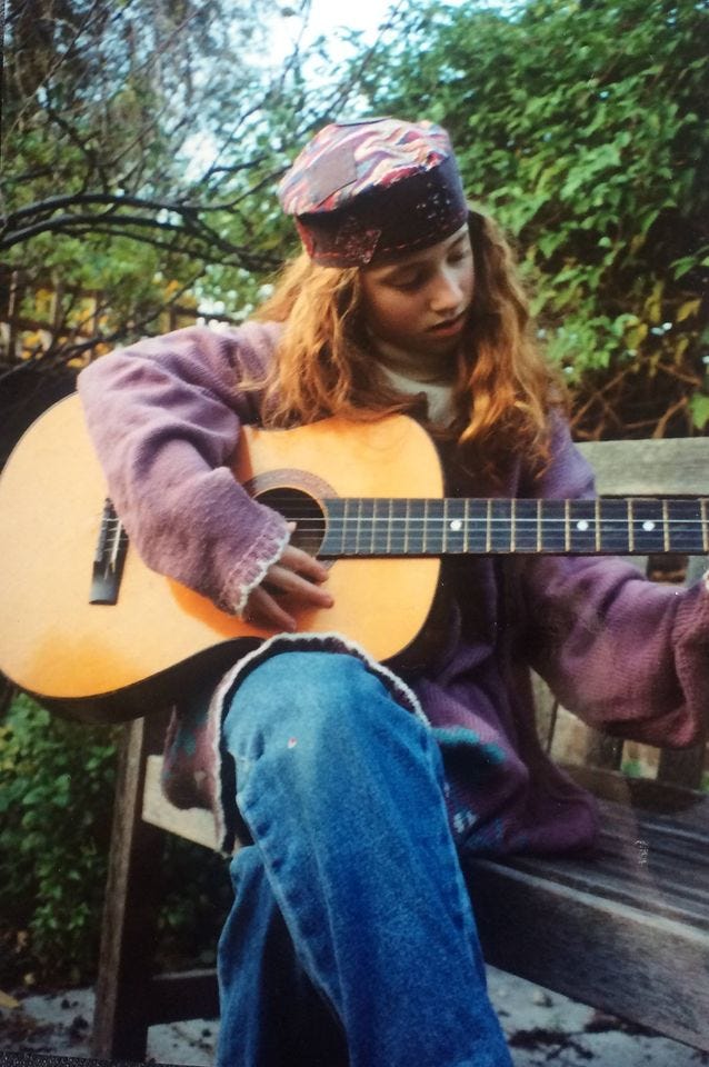 A young girl plays the guitar wearing a hand made hat