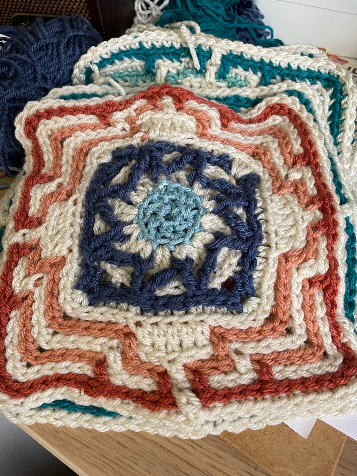 several intricately crosheted squares in colors of red and white and blue. There is a star shaped pattern in the middle and mosiac patterns around the edges