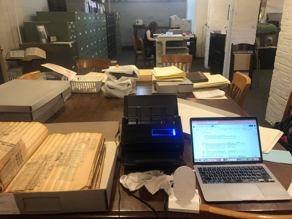 In the basement of the Evanston History Center, situated on a table are a box of newspaper clippings, my scanner, my phone charger, my open laptop, and my white, lint-free gloves to safely handle the archived material