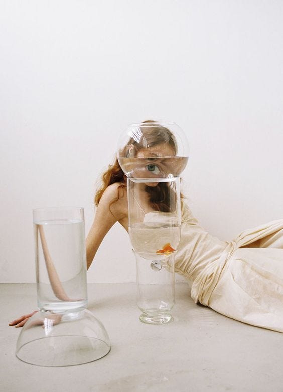 This may contain: a woman laying on the ground next to a glass filled with water and goldfish