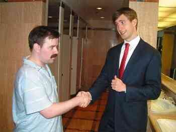 Two men shake hands in a public bathroom