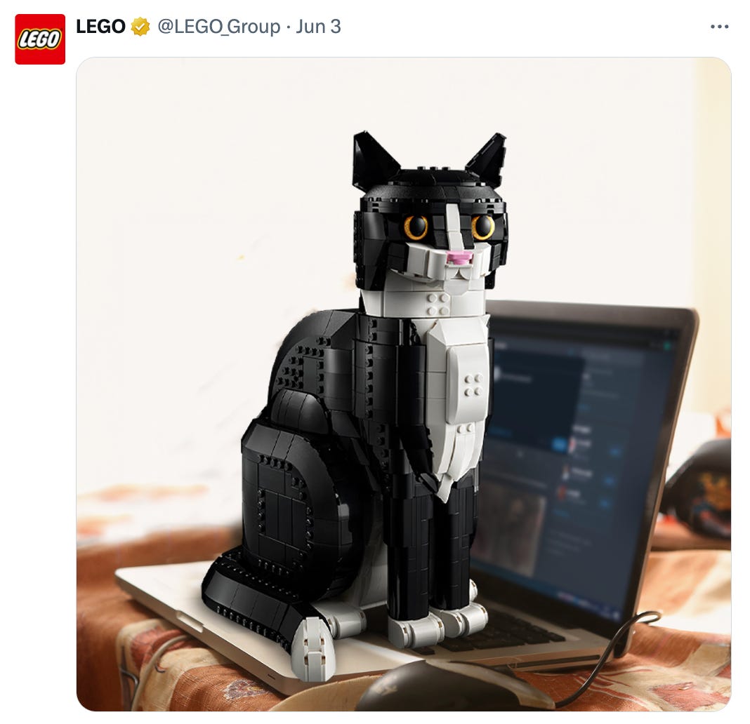 Tweet from @LEGO_Group that features an image of a black and white LEGO cat sitting on the keyboard of an open laptop.